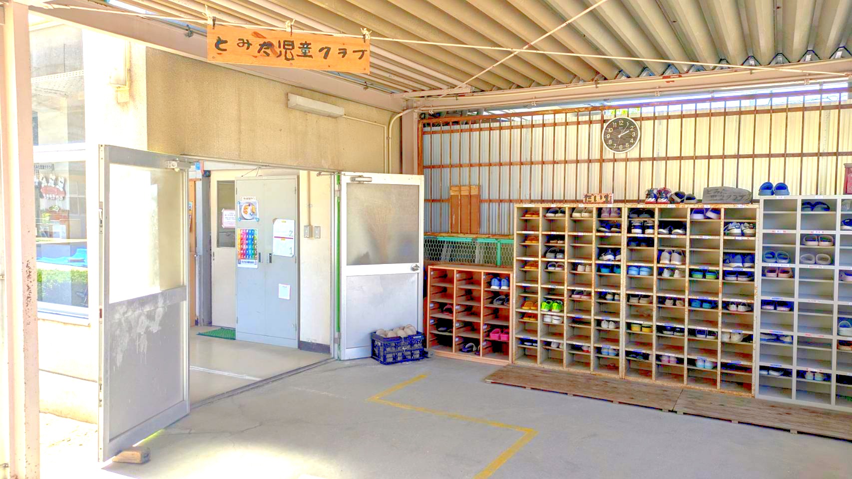 とみた児童クラブの玄関。手書きの看板と、ずらりと並んだ下駄箱