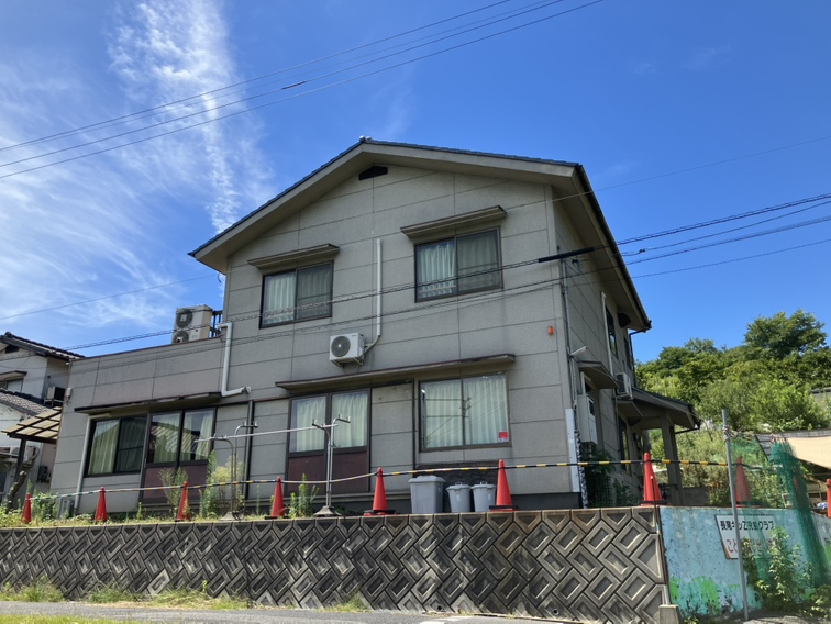 2階建ての建物。手前のブロック塀ぞいに、赤いコーンがずらりと並んでいる
